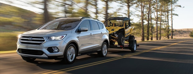 a silver ford escape towing a construction vehicle drives through an empty road