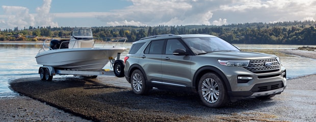 a grey ford explorer with a boat attached to the back parked on a sandy area next to water 