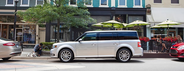 a white ford flex parallel parked in a shopping area
