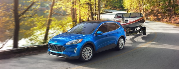 a blue ford escape towing a boat down a road flocked by gold leafed trees 