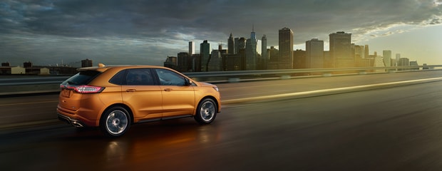 an orange ford edge drives into a city while its cloudy