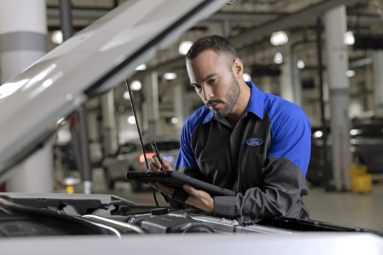A mechanic looks down into an engine as he checks something off of his clipboard 